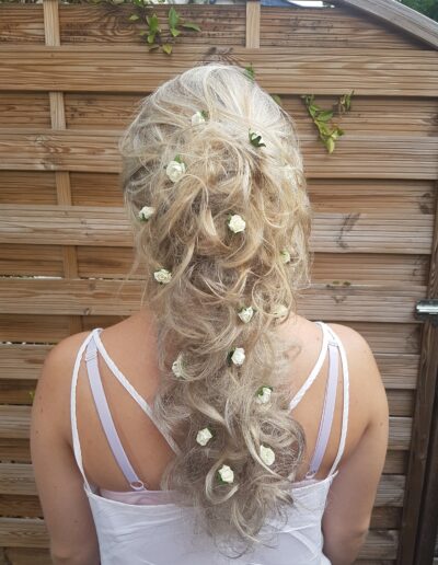 Coiffure blonde relevée, bouclée et ornée de petites fleurs