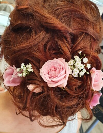 Coiffure attachée sur cheveux roux, décorée de roses et de petites fleurs blanches