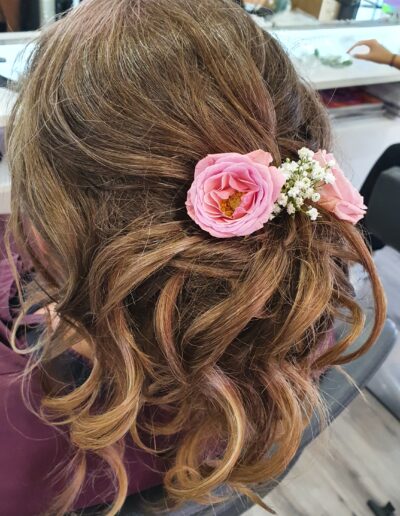 Coiffure brune ondulée et attachée avec une fleur rose